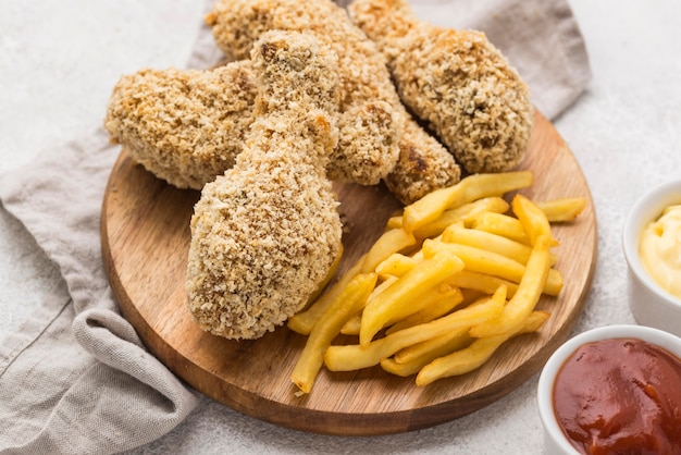 Foto gratuita alto ángulo de muslos de pollo frito con papas fritas y salsas