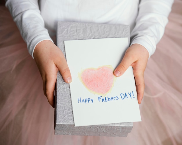 Foto gratuita alto ángulo de niña sosteniendo presente y tarjeta para el día del padre