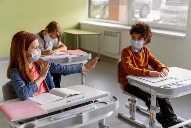 Alto ángulo de niños con máscaras médicas manteniendo la distancia en el aula