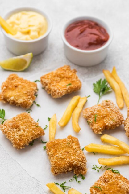 Alto ángulo de nuggets de pollo frito con salsas y papas fritas