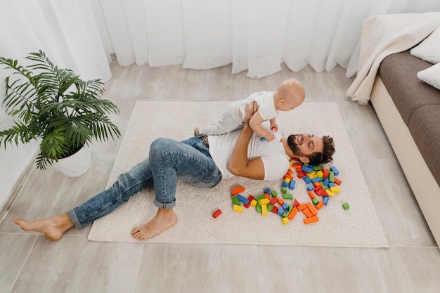 Alto ángulo de padre jugando en el suelo en casa con el bebé