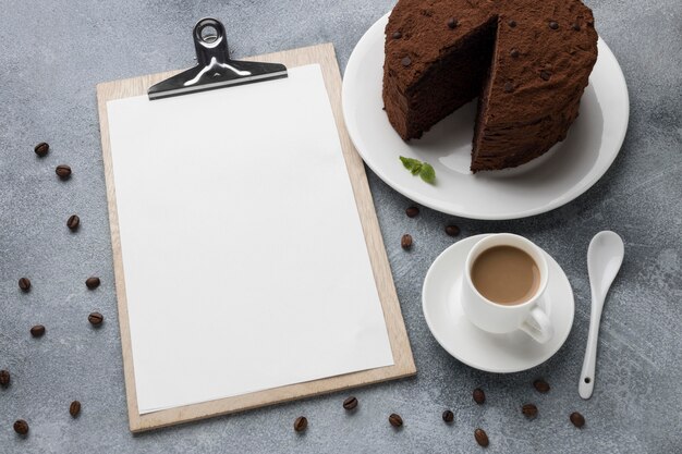 Alto ángulo de pastel de chocolate con bloc de notas y café