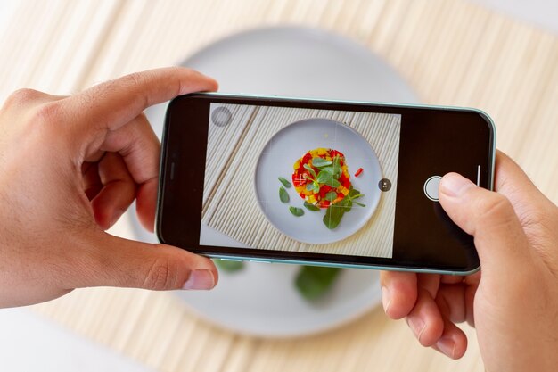 Alto ángulo de la persona que toma la foto de la comida en el plato con el teléfono inteligente