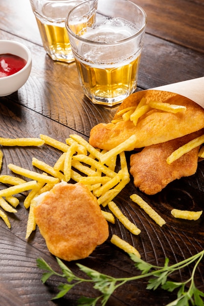 Alto ángulo de pescado y patatas fritas en cono de papel con cerveza