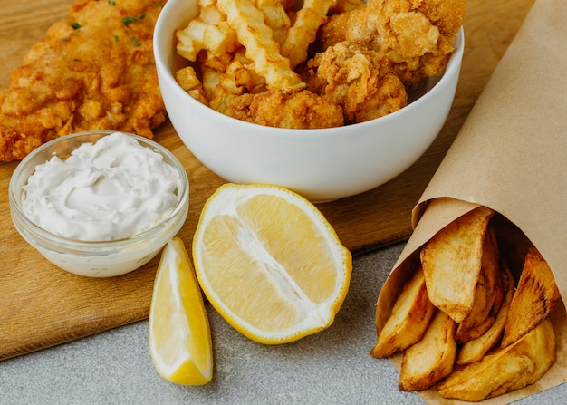 Alto ángulo de pescado y patatas fritas en un tazón y envoltura de papel con limón