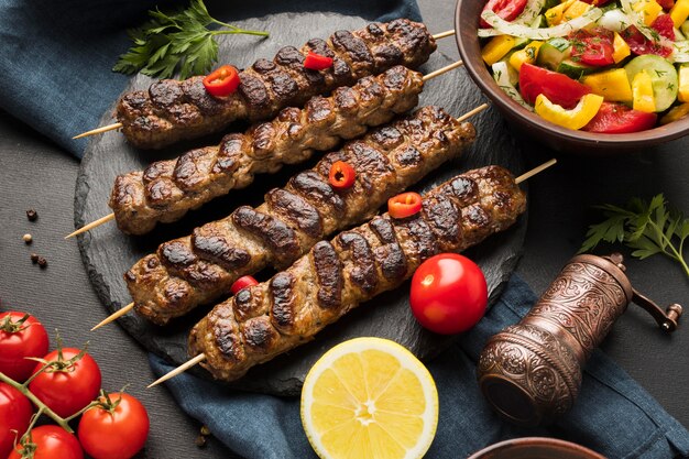 Alto ángulo de sabroso kebab en pizarra con otro plato y tomates