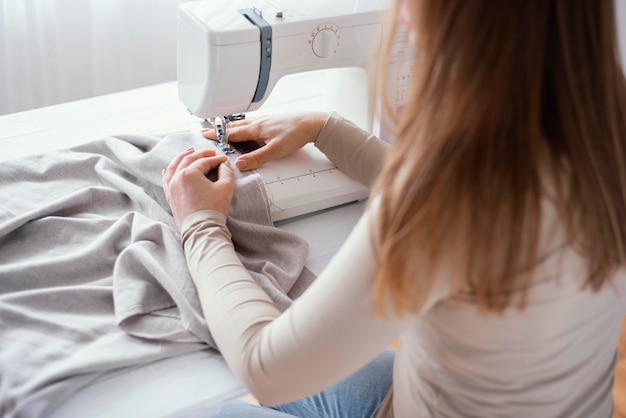 Alto ángulo de sastre femenino con máquina de coser y tela