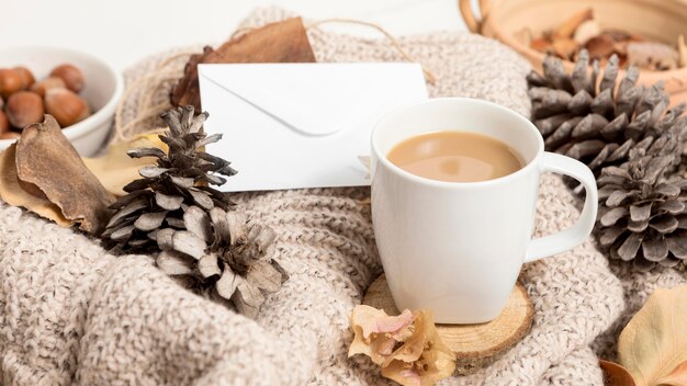 Alto ángulo de taza de café con hojas de otoño y piñas