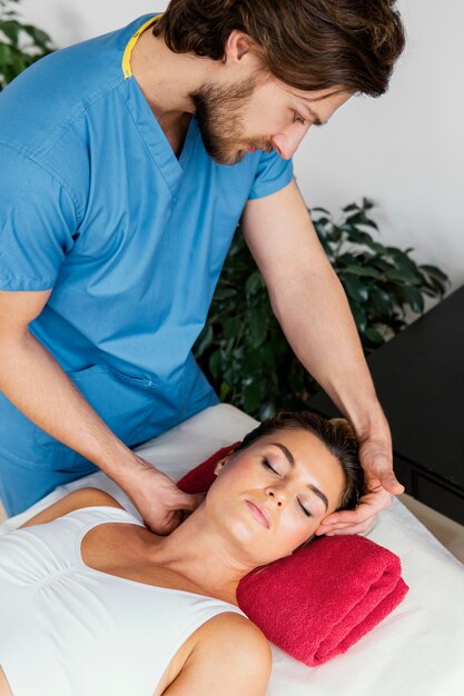 Alto ángulo del terapeuta osteopático masculino que controla la columna del cuello del paciente femenino