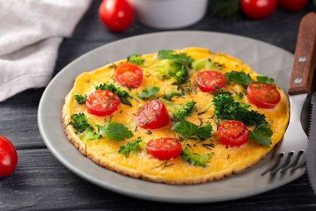 Alto ángulo de tortilla para el desayuno con tomates y hierbas.