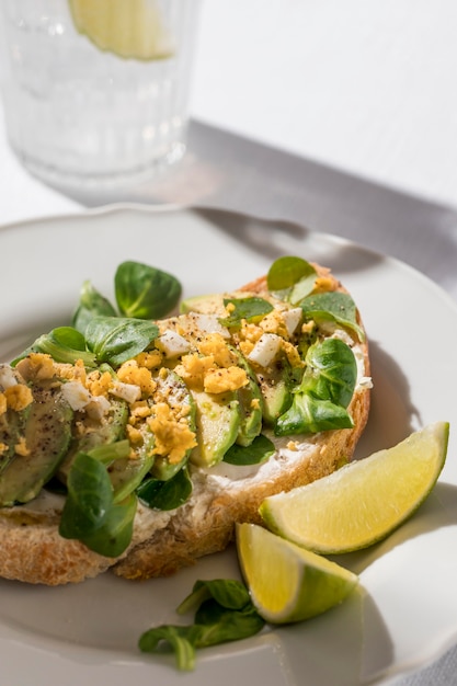 Alto ángulo de tostadas de aguacate en un plato con un vaso de agua helada y limas