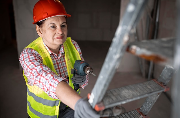 Alto ángulo de trabajadora de la construcción con taladro eléctrico