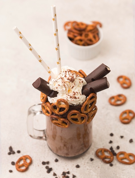 Alto ángulo de vaso de batido de chocolate con pretzels y pajitas