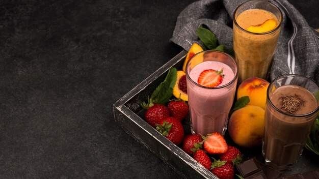 Alto ángulo de vasos de batido en bandeja con chocolate y frutas