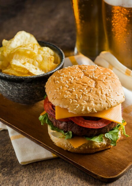 Alto ángulo de vasos de cerveza con hamburguesa con queso y patatas fritas