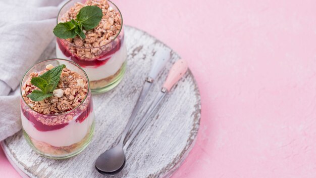 Alto ángulo de vasos de yogurt con cereales y cucharas