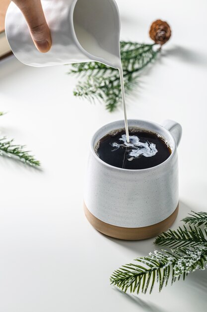 Alto ángulo de verter crema de mano en taza de café