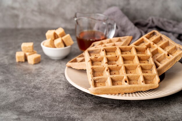 Alto ángulo de waffles en plato con terrones de azúcar y jarabe