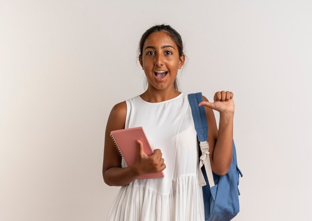 Alumna joven alegre con mochila sosteniendo portátil y apunta a sí mismo