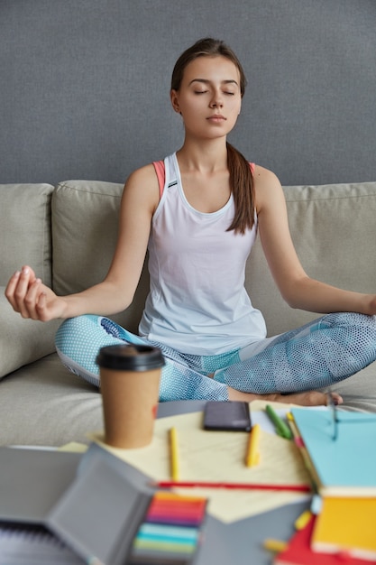 Foto gratuita alumna sentada en posición de loto, siente paz respirando, encuentra inspiración en la meditación, bebe café