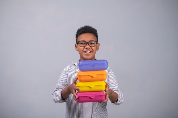 Alumno sonriente demostrando coloridos recipientes de plástico para alimentos