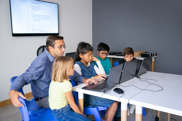 Alumnos multiétnicos haciendo tareas con la ayuda del profesor