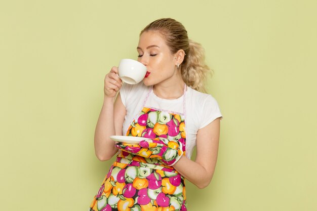 Ama de casa joven en camisa y capa de color bebiendo té en verde