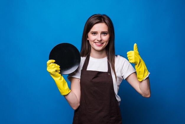 Ama de casa joven en guantes mostrando esponja y plato limpio aislado