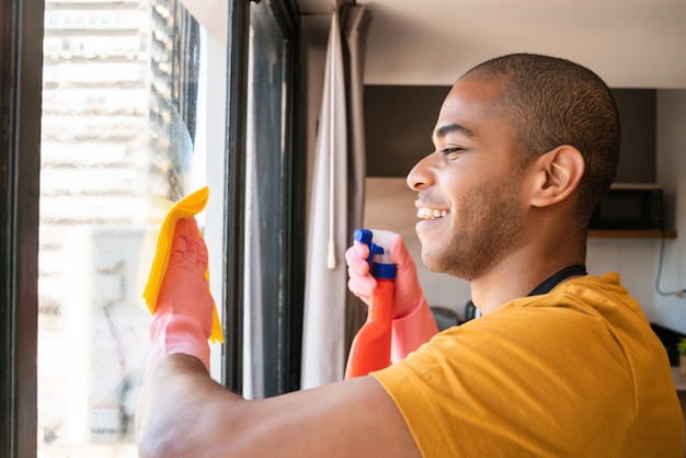 Ama de casa masculina que limpia la ventana de cristal en casa.