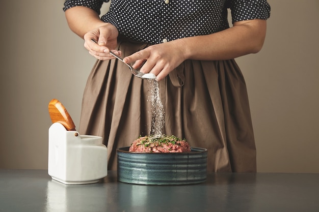 Foto gratuita ama de casa mujer irreconocible agrega un poco de sal en la carne picada en un recipiente de cerámica sobre la mesa azul