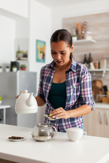 Ama de casa preparando drinkg caliente en la cocina con hierbas aromáticas en la tetera