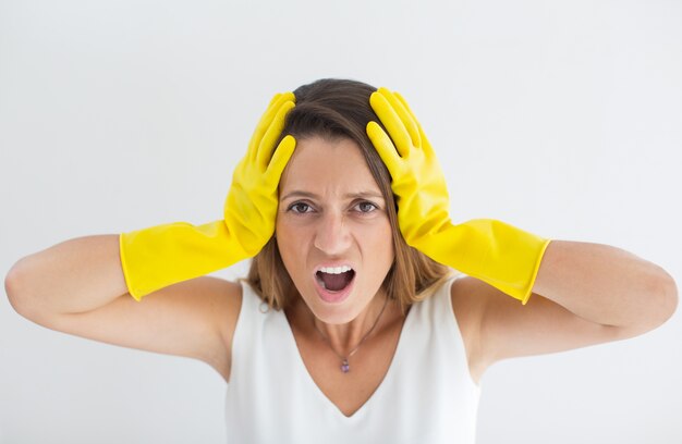 Ama de casa tensionada en guantes sosteniendo la cabeza en manos