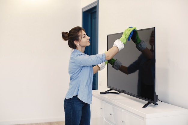 Ama de casa trabajando en casa. Dama con camisa azul. Mujer limpia TV.