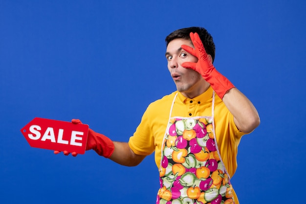 Foto gratuita ama de llaves masculina vista frontal en camiseta amarilla con cartel de venta abriendo los ojos en el espacio azul