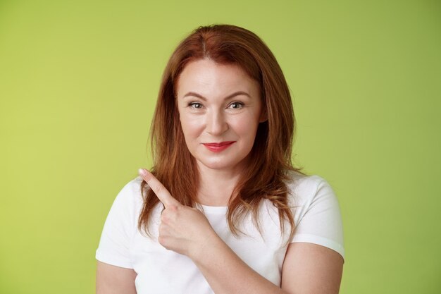 Amable alegre mujer de mediana edad pelirroja s camiseta blanca sonriendo modestamente aseguró dar consejos apuntando hacia la esquina superior izquierda