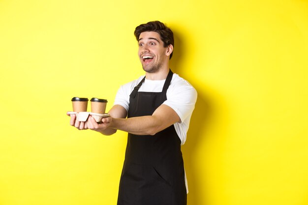 Amable barista en delantal negro dando orden de comida para llevar sosteniendo dos tazas de café y sonriendo ...