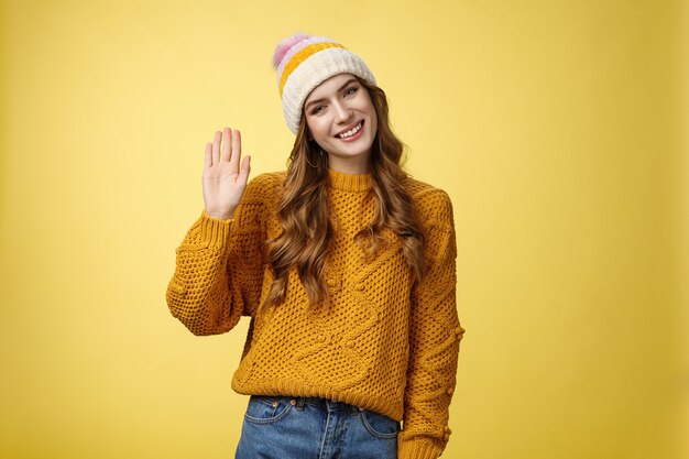 Amable encantadora mujer joven sonriente inclinando la cabeza mirada saliente agitando la mano hola hola gesto saludar ...