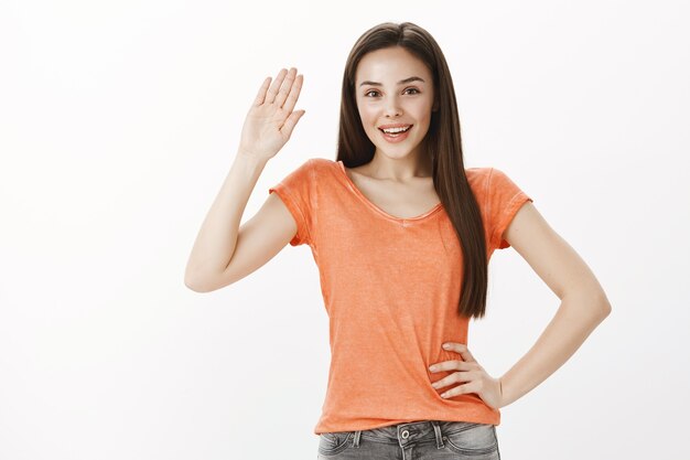 Amable hermosa joven diciendo hola, saludando con la mano gesto de saludo, persona bienvenida