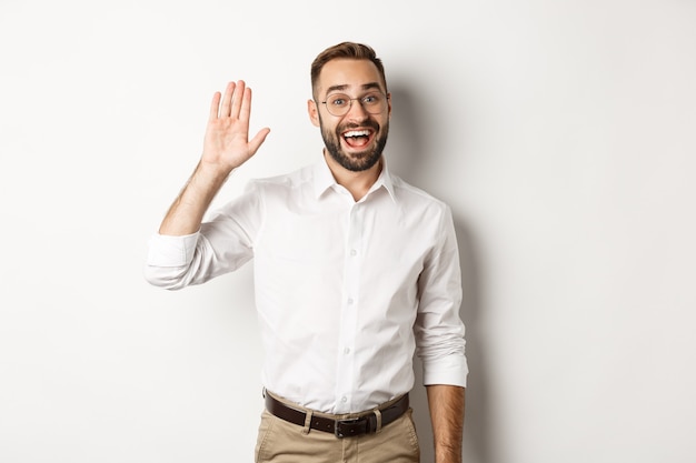 Amable hombre sonriente con gafas diciendo hola, saludando con la mano, de pie