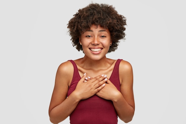 Amable novia de piel oscura mantiene las manos en el pecho, expresa modales amigables