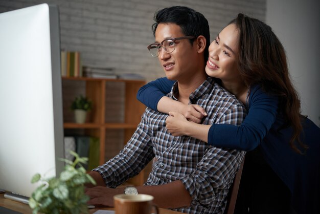 Amada esposa abrazando a su esposo por la espalda mientras él está trabajando en la computadora