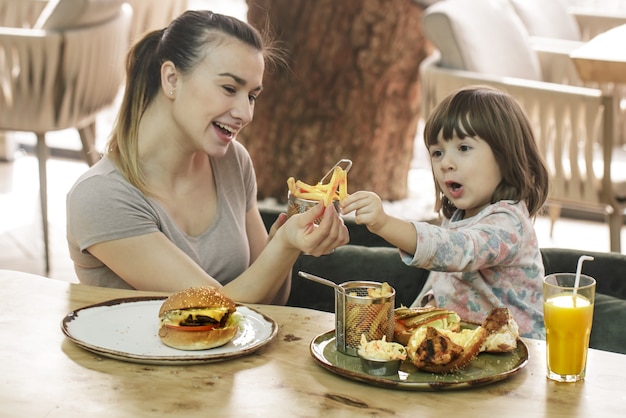 Amando familia. Mamá con linda hija comiendo comida rápida en un concepto de cafetería, familia y nutrición