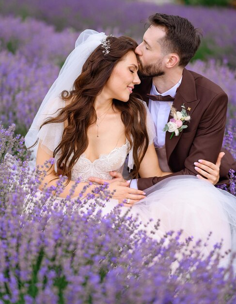 Amando a los recién casados posando en el prado de lavanda y abrazándose