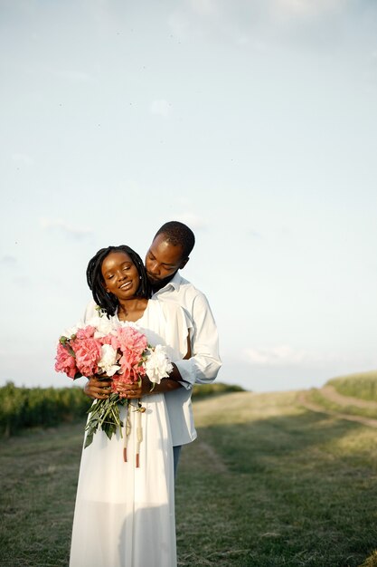 Amantes afroamericanos abrazándose en un campo. Mujer sosteniendo flores.