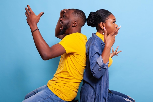 Foto gratuita amantes irritados en conflicto peleando y sentados espalda con espalda, gritándose y estando en desacuerdo. pareja con problemas de relación y crisis discutiendo frente a la cámara.