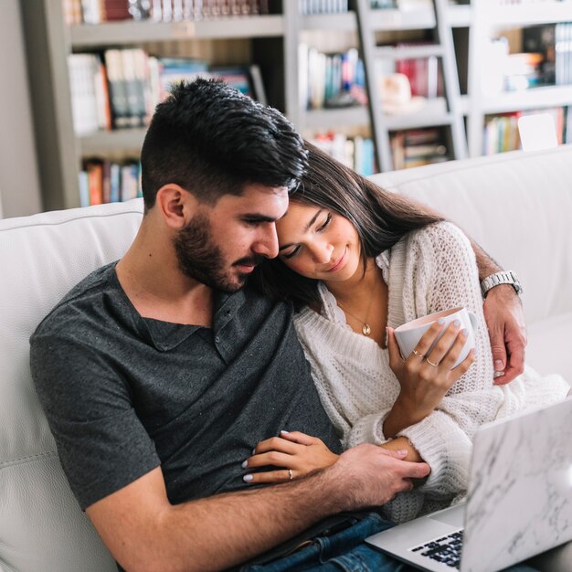 Amantes de la joven pareja sentada en el sofá mirando portátil