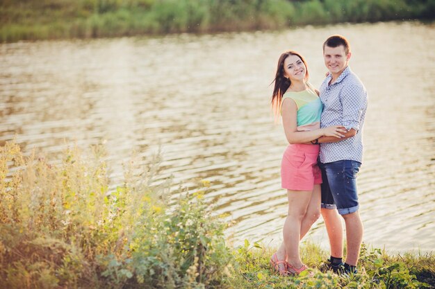 Amantes en un lago Pareja joven enamorada sentada en el suelo del parque cerca del agua mientras estos jóvenes tocan la guitarra al atardecer