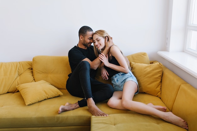 Amantes en una ropa de casa abrazándose tiernamente con los ojos cerrados en el sofá. Abrazo romántico, caras felices, sensualidad, ternura, amor.