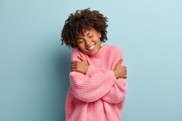 Foto gratuita Ámate a ti mismo concepto. foto de hermosa mujer sonriente se abraza a sí misma, tiene alta autoestima, cierra los ojos por placer