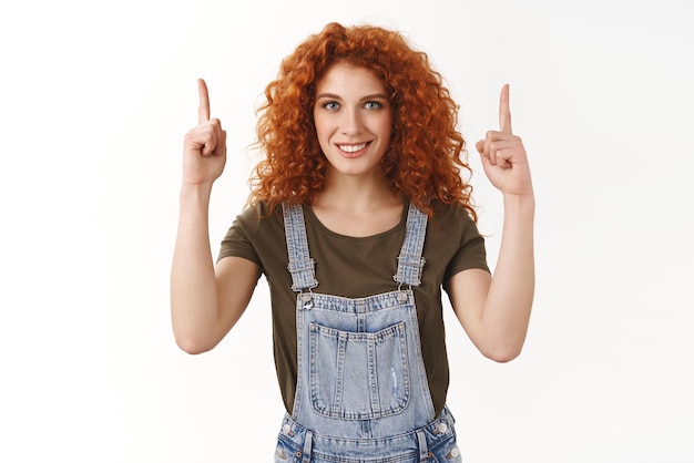 Foto gratuita la ambiciosa actriz pelirroja que sueña con convertirse en la mejor apuntando con el dedo hacia arriba con una expresión de confianza sonriendo con una sonrisa dentada blanca determinada a lograr el éxito de pie en un fondo blanco